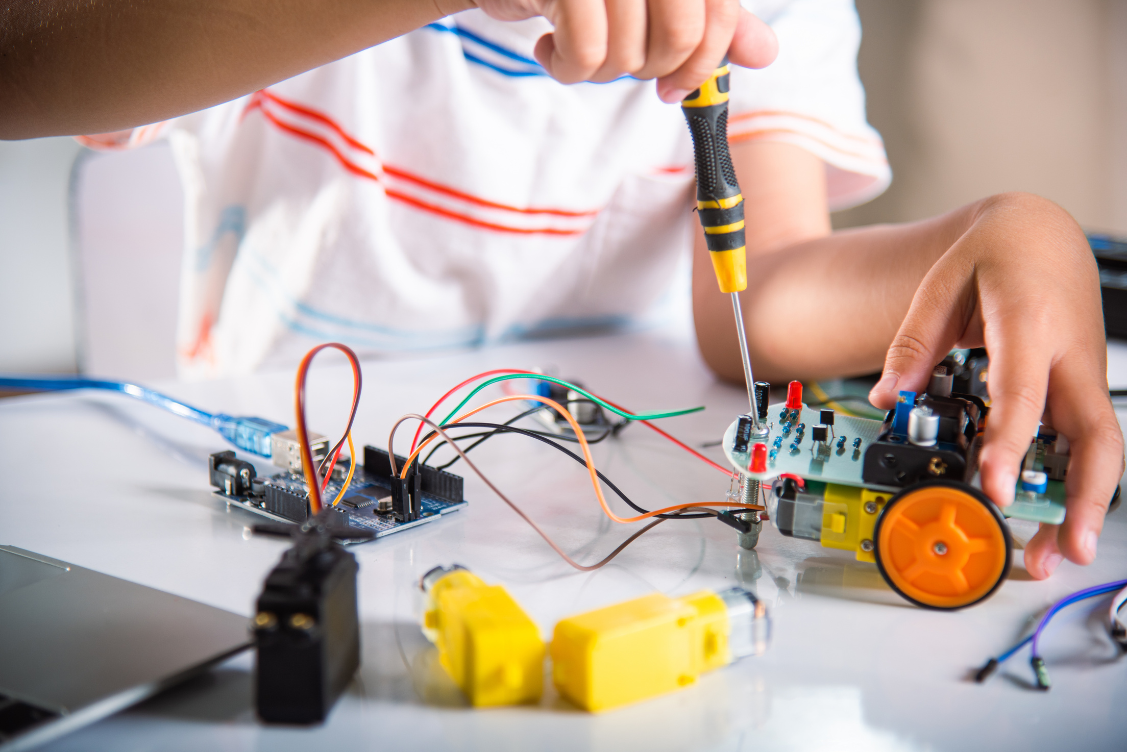 Asian kid boy assembling the Arduino robot car homework proj